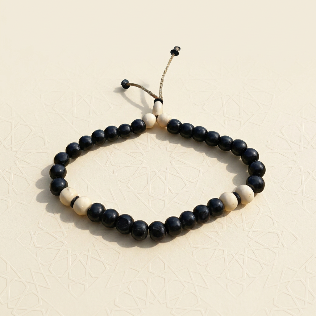 Adjustable 33-bead dhikr bracelet with glossy black beads, ivory accent beads and a braided drawstring cord, on ivory with a subtle Islamic geometric pattern
