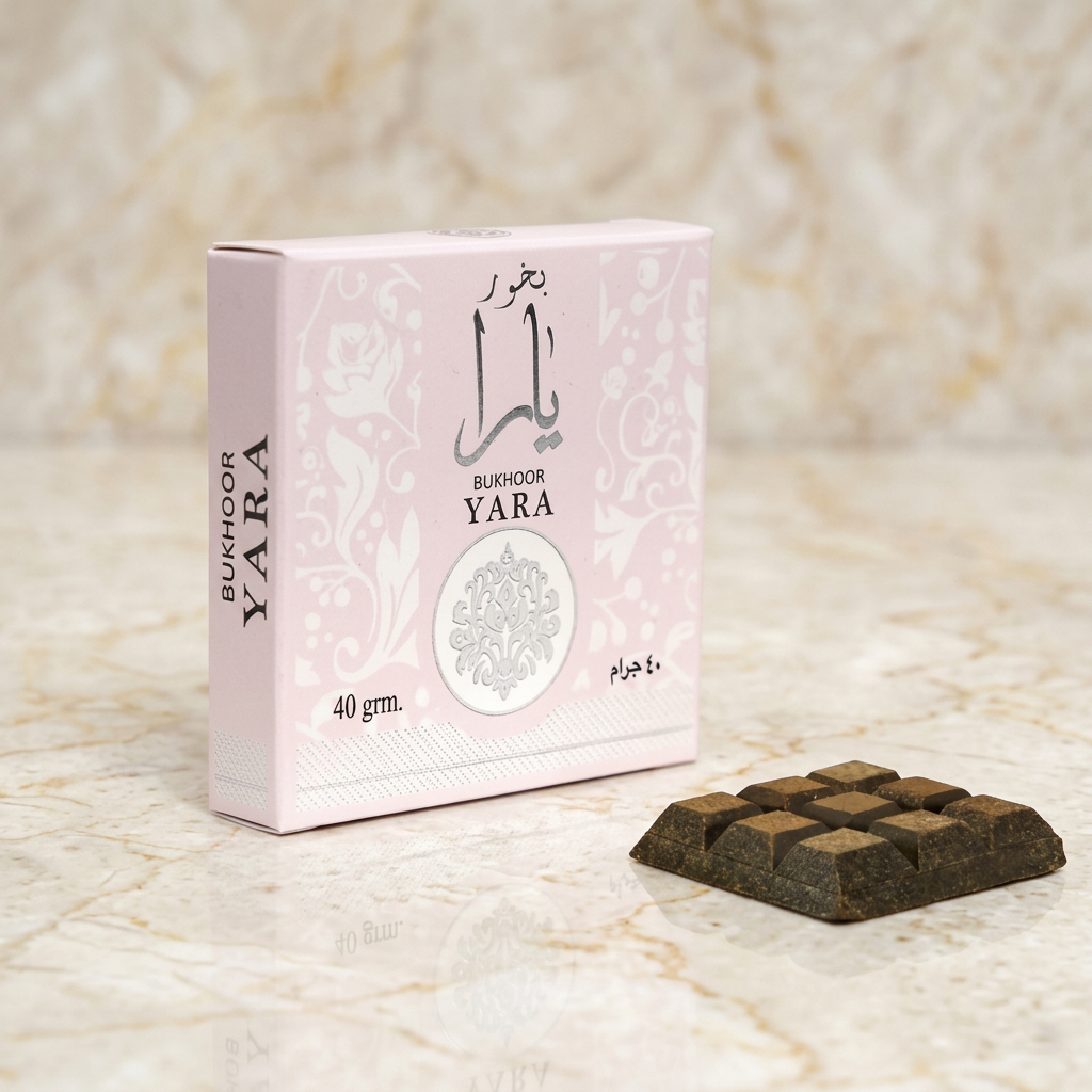 Pink Bukhoor Yara 40 gram box with Arabic calligraphy and silver medallion, beside a block of dark bukhoor incense, on cream marble